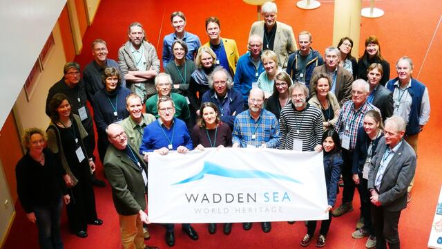 Participant of the CVI workshop with Wadden Sea World Heritage flag photographed from higher ground. © CWSS/ Fransiska Neigenfind.