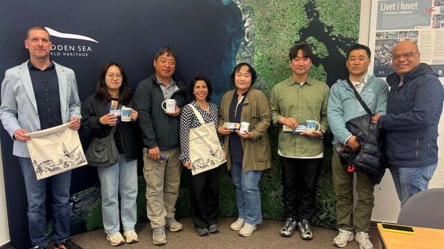 A group of people standing in front of a banner depicting the Wadden Sea from satellite. © CWSS.